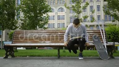 有魅力的年轻人坐在公园的长凳上，用手机听音乐，然后拿起<strong>拐杖</strong>和<strong>拐杖</strong>。